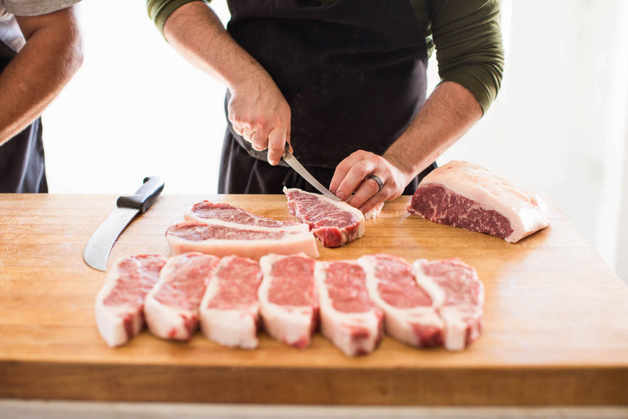 Butcher cutting NY Strip steaks on butcher block
