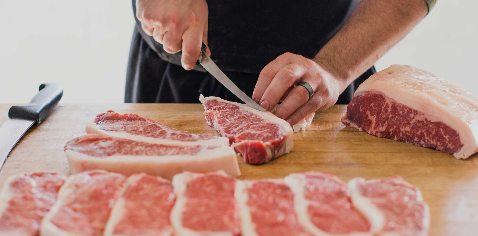 Butcher trimming dry-aged steaks on butcher block